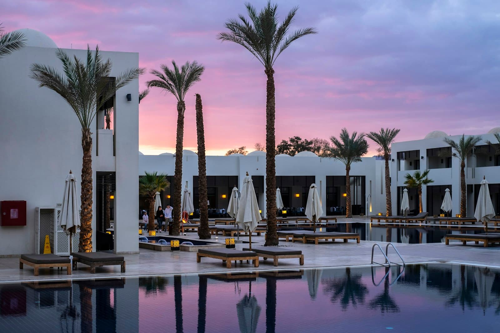 Domed resort courtyard with palms and a still pool at dusk